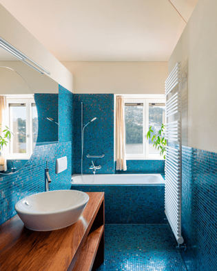Blue tiled bathroom with bathtub/shower unit and bowl sink atop a simple wooden cabinet